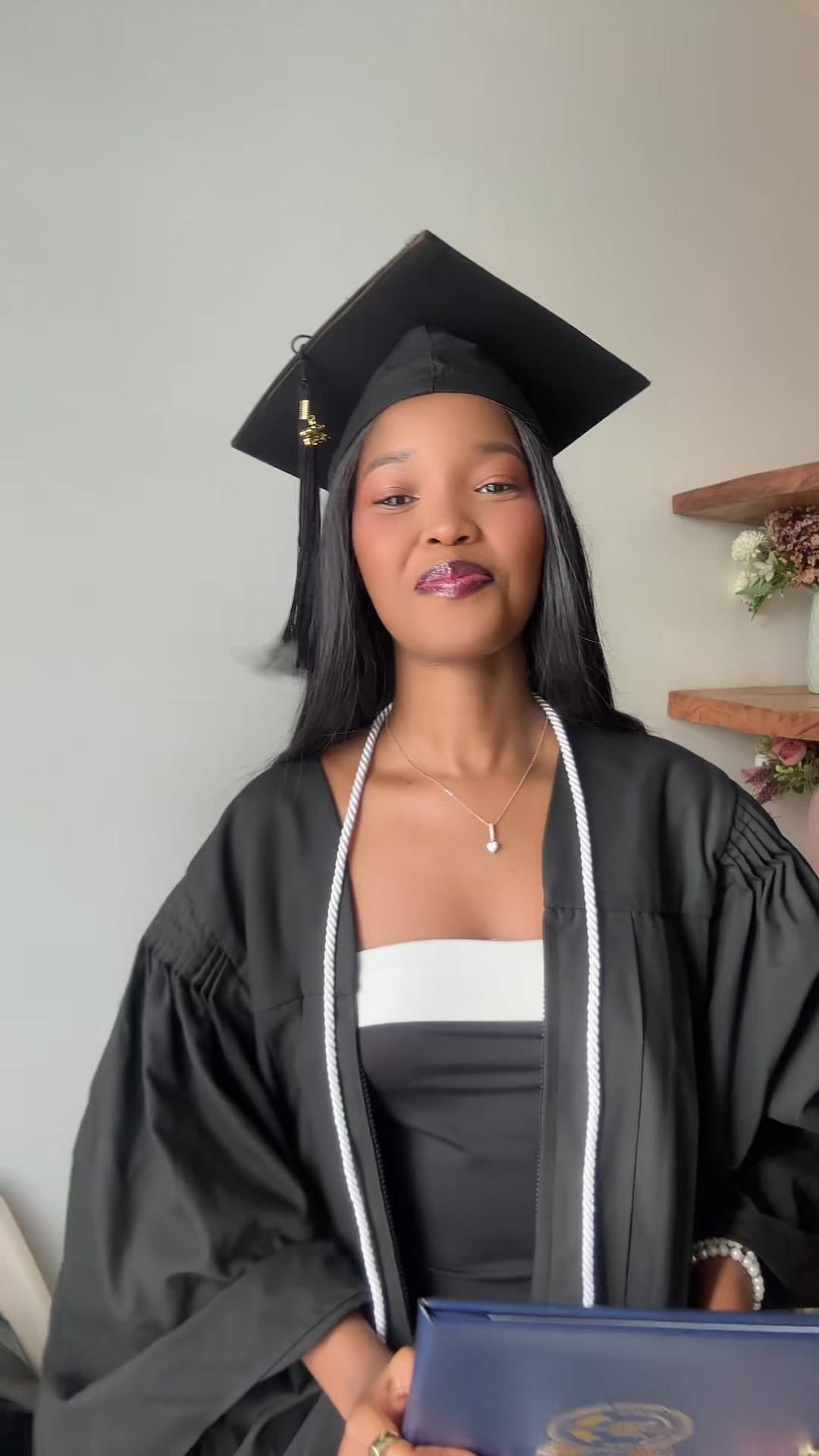 Primrose in her graduation cap and gown holding her degree folder